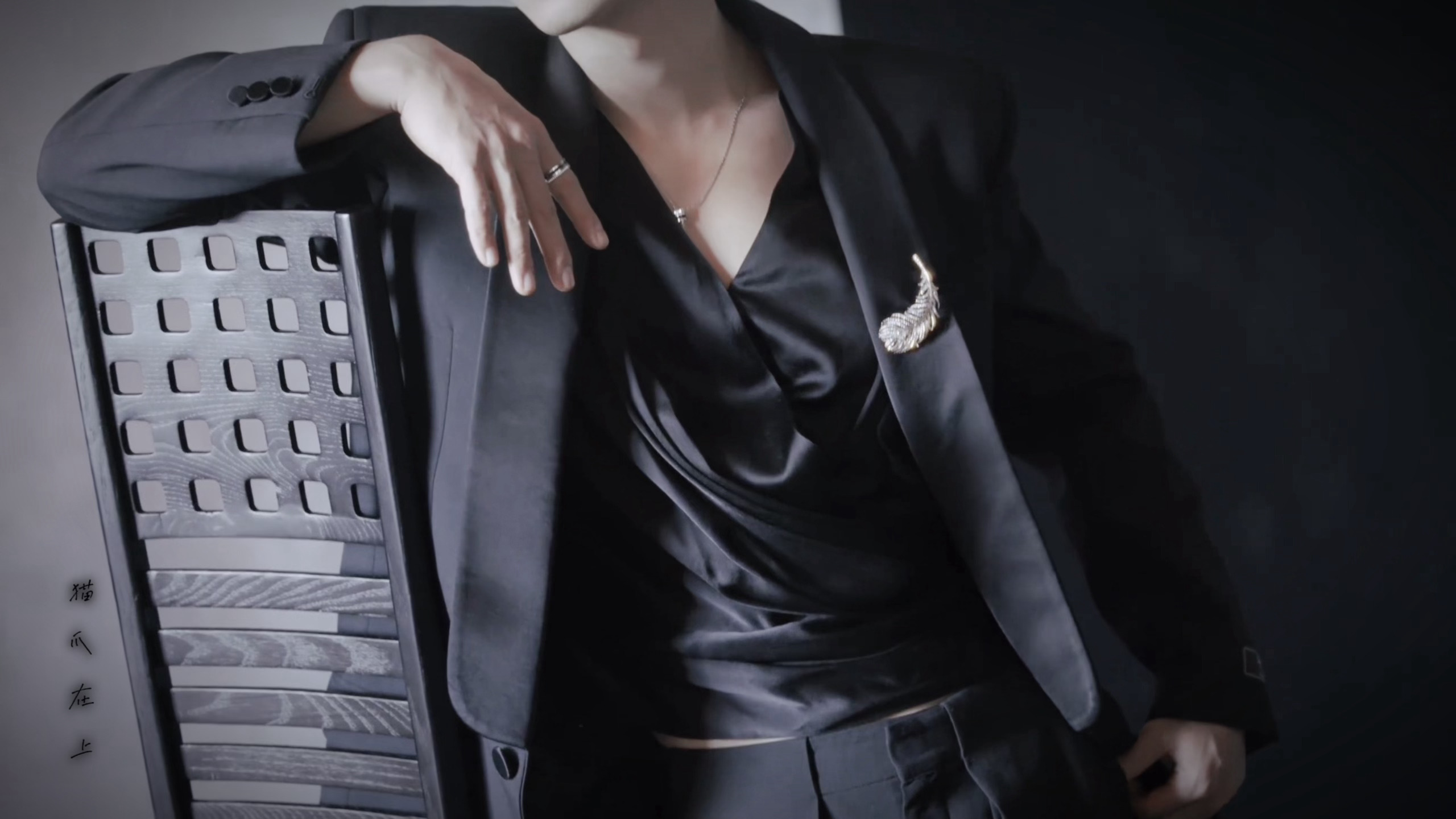 Xiao Zhan in a black Balmain suit with a feather pin, leaning against a chair – a close-up of his outfit
