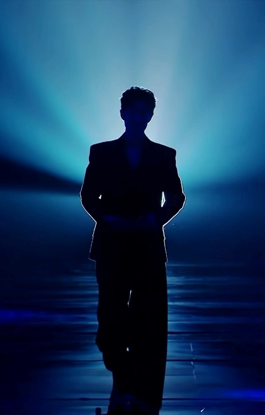 Xiao Zhan on stage during his narration segment, holding a microphone and engaging the audience