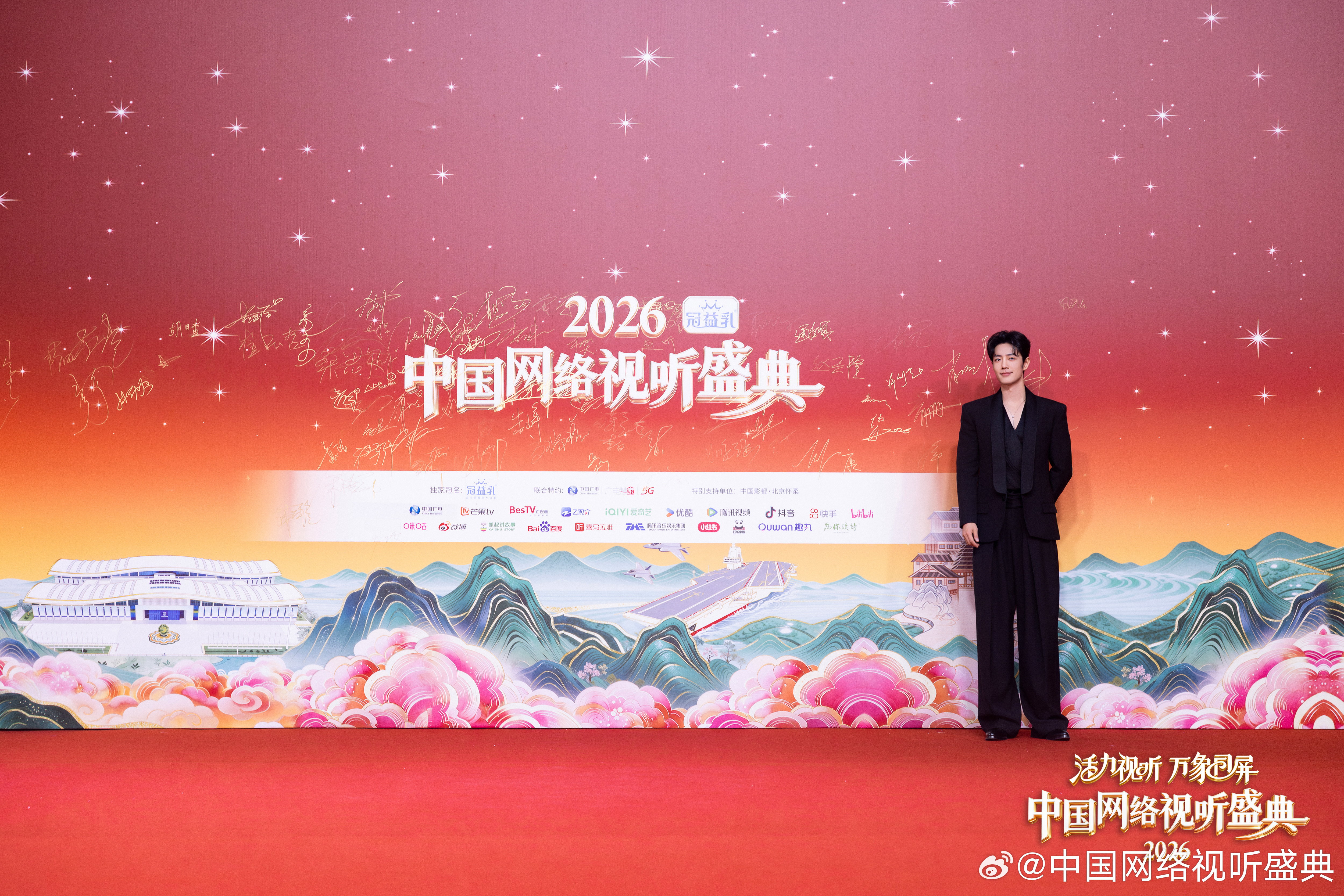 Xiao Zhan poses on the red carpet at the 2026 China Network Audiovisual Gala, wearing a sleek black suit with a feather brooch